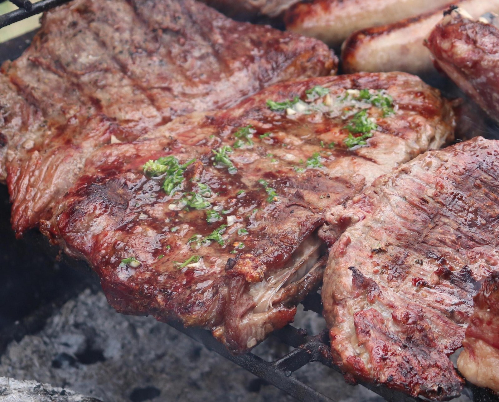 Cortes de carne a la parrilla con chimichurri fresco, sobre brasas de carbón